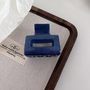 Detailed top view of a navy blue marble square hair claw clip on a linen wooden tray