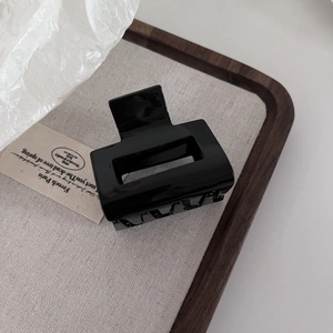 Detailed close-up of a glossy black acetate hair claw clip on a minimalist wooden tray
