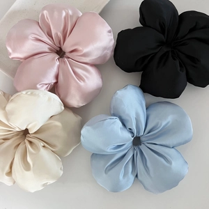 Détail de quatre chouchous fleurs en satin rose, noir, beige et bleu avec texture soyeuse
