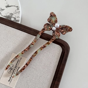 Detailed macro view of U-shaped acetate hair pin with butterfly motif and faux pearls