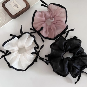 Vue détaillée de trois chouchous en organza rose, blanc et noir avec nœuds décoratifs