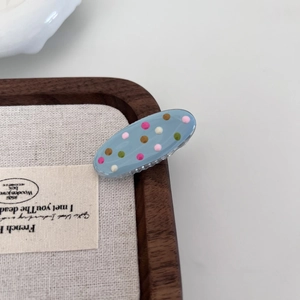 Close-up of a small light blue resin hair clip with colorful polka dots on a wooden tray