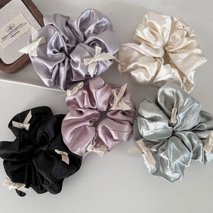 Macro shot of five satin scrunchies with shiny metallic texture and tiny white bows