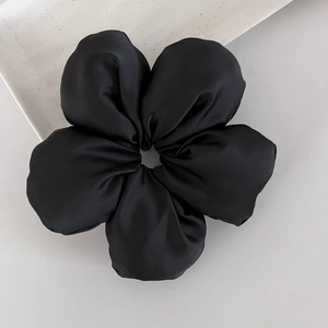 Détail d'un chouchou fleur en satin noir sur un plateau de présentation minimaliste