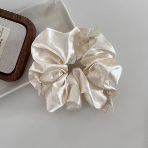 Close-up of champagne satin scrunchie with delicate bow details and silk texture