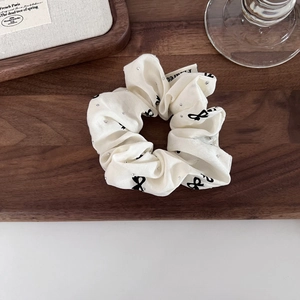 Elegant cream fabric scrunchie with black bow prints and sparkling rhinestones for hair