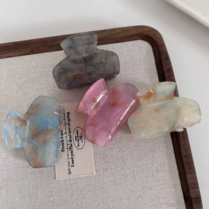 Set of four shimmering acetate hair claws in assorted marble patterns on a wooden tray
