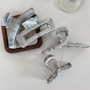 Detail showing various marble pattern acetate hair claws on a minimalist wooden tray