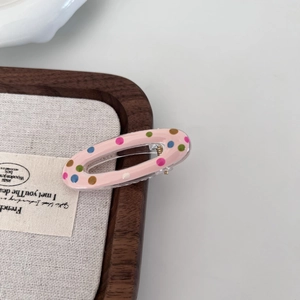 Detail showing a pink oval hair clip with colorful polka dots on a wooden tray display