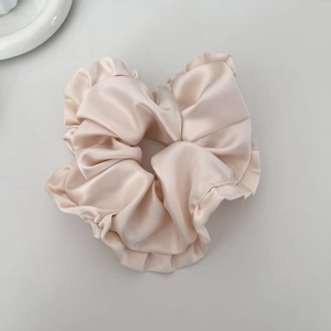 Close-up detail of champagne satin ruffled scrunchie with soft metallic silk texture