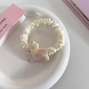 Nahaufnahme eines cremefarbenen Satin-Haargummis mit buntem Regenbogen-Hasen-Anhänger