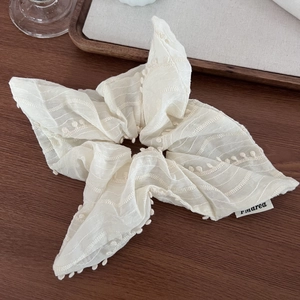 Elegant cream white fabric scrunchie with fringe embroidery on a dark wooden background