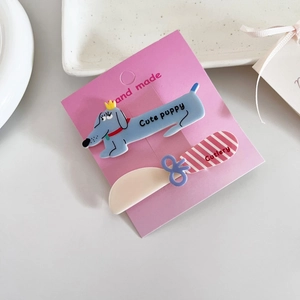 Détail de barrettes chiot bleu et rayures roses sur une carte artisanale violette
