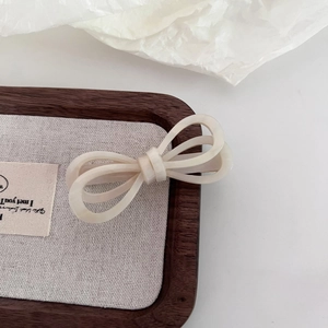Elegant cream acetate bow hair clip with marble pattern on a minimalist wooden tray