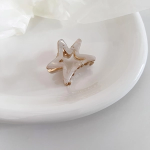 Detail of star-shaped acetate hair claw clip with marble texture and gold metal teeth