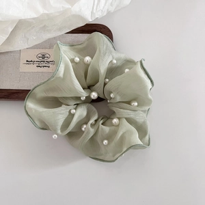 Detail eines hellgrünen Organza-Haargummis mit eleganten künstlichen Perlenverzierungen