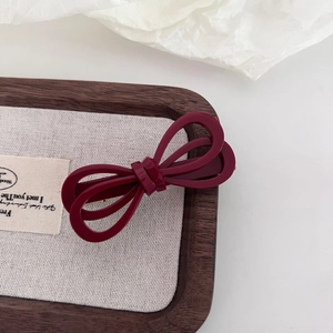Detail of a dark red bow hair clip with a layered design on a textured display tray