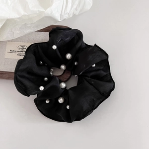 Detail eines schwarzen Chiffon-Haargummis mit weißen Perlen auf einem Holztablett