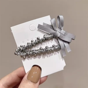 Détail d'une pince à cheveux perlée argentée avec un nœud en tissu gris sur carte
