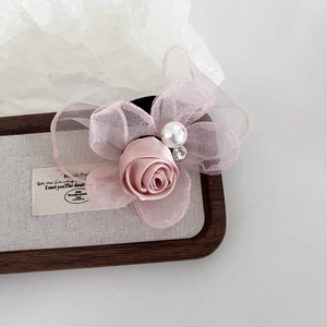 Pink satin rose hair tie with organza petals, pearl and rhinestone on a wooden tray