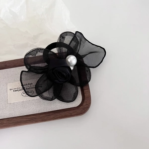 Detail of a black mesh rose hair scrunchie with a central pearl on a wooden tray