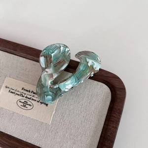Detailed macro view of an acetic acid hair claw clip with green marble texture and gold script