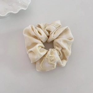 Detail showing yellow plaid scrunchie fabric with intricate bow embroidery and soft texture