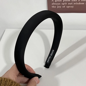 Détail d'un serre-tête en satin noir avec étiquette cousue à la main sur la face interne