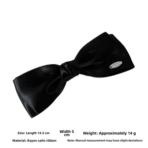 Detail showing 14.5cm length and 5cm width of the black satin bow hair clip with silver tag