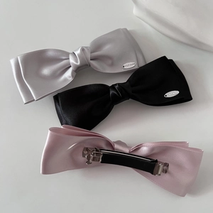 Three-piece set of satin bow hair clips in grey, black, and pink with metal brand tags
