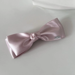 Detail of pink satin bow hair clip featuring a small oval silver metal logo tag
