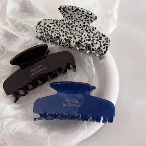 Three medium acetate claw clips in dark coffee, navy, and spotted patterns with gold logo