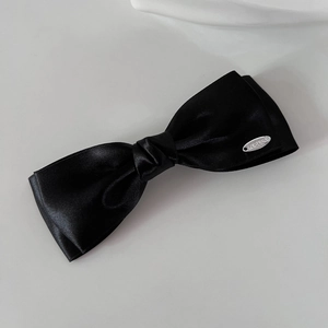 Detailed view of the double-layered black satin bow hair clip with silver metal tag