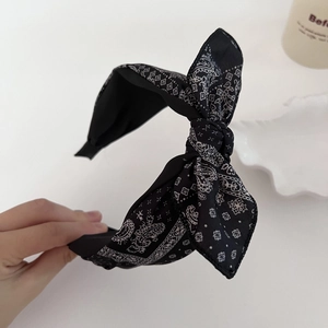 Close-up detail of a wide black paisley print headband with a stylish knotted bow