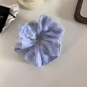 Dettaglio dell'elastico per capelli a righe azzurre con fiori 3D su sfondo beige