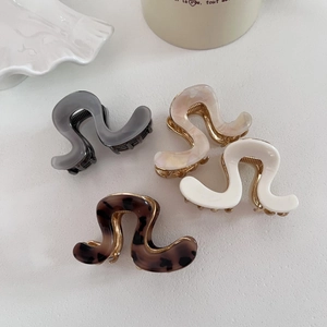 Detail of four acetate wave-shaped hair claws in marble, white, grey, and tortoiseshell
