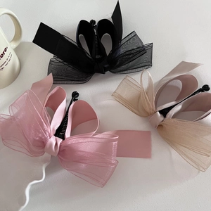 Détail de trois barrettes banane en organza avec nœuds en noir, rose et champagne