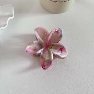 Détail d'une pince à cheveux fleurie marbrée rose et vert sur une surface blanche