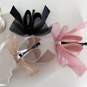 Gros plan de pinces nœuds en tulle et satin superposés en noir, rose et champagne clair