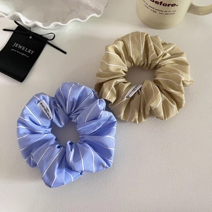 Close-up of blue and khaki striped fabric scrunchies with text labels on a white desk