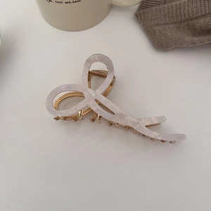Close-up of elegant cream bow hair claw with marble texture and gold metal base