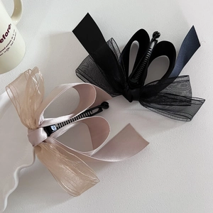Détail de pinces à cheveux à nœuds en résille noir et champagne sur fond blanc