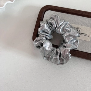 Metallic silver scrunchie with pleated texture on a wooden tray with a minimalist design