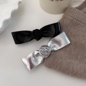 Vue détaillée des barrettes à fleurs en cuir argenté et noir sur une table blanche