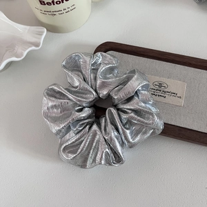 Close-up of metallic silver pleated scrunchie with high-shine texture on a wood tray