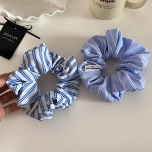 Detail shot of two blue striped fabric scrunchies with woven labels on a white tray