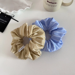 Detailed view of striped fabric scrunchies in blue and khaki with elegant label tag