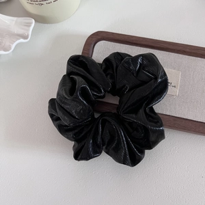 Macro view of a large black scrunchie with high-gloss leather texture and thick pleats