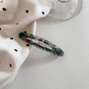 Detail of hollow oval acetate hair clip with green and purple marble texture and silver clip