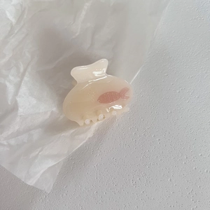 Detail view of a cream resin hair claw clip with a pink fish design on white texture